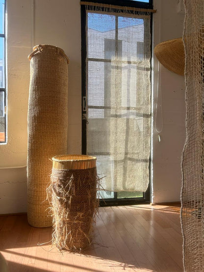 Tall floor standing storage basket, shown with a double height column basket. Both natural colored. Made in Ghana from local sustainable materials.