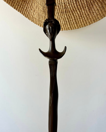 A vintage, iron 'Tête de femme' style floor lamp in the manner of Alberto Giacometti, paired with a Twenty One Tonnes handwoven, wide brimmed, natural colored light shade.