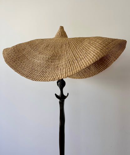 A vintage, iron 'Tête de femme' style floor lamp in the manner of Alberto Giacometti, paired with a Twenty One Tonnes handwoven, wide brimmed, natural colored light shade.