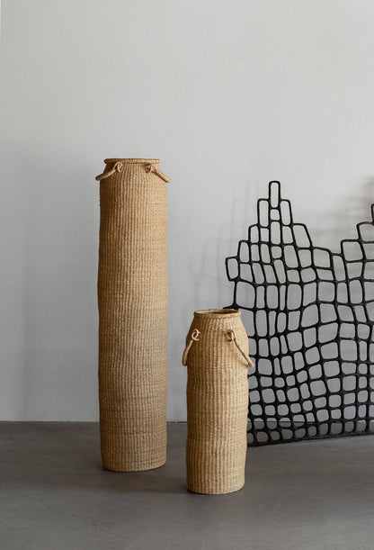 Very tall column-shaped baskets with two handles. More sculpture than storage, these hand woven baskets are made in Ghana from sustainable local grass.