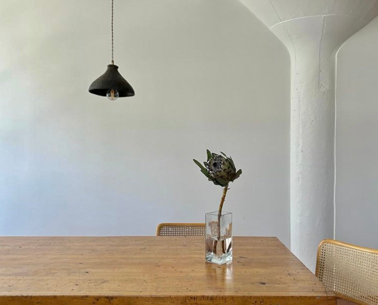 The Mud Pendant lightshown over a dining table with a vase and flower.