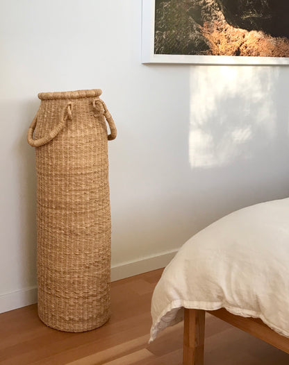 A tall column-shaped basket with two handles. More sculpture than storage, these handwoven baskets are made in Ghana from natural materials.