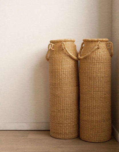 A tall column-shaped baskets with two handles. More sculpture than storage, these handwoven baskets are made in Ghana from natural materials.