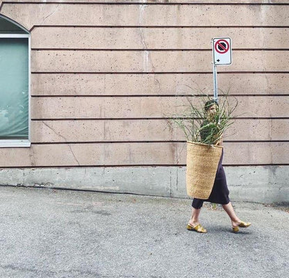 Woman carrying a large basket with plants.