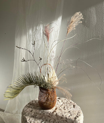 A small smoked bamboo basket with handle and dried flowers. Basket handcrafted and hand woven by Japanese artist Mie Kodama.