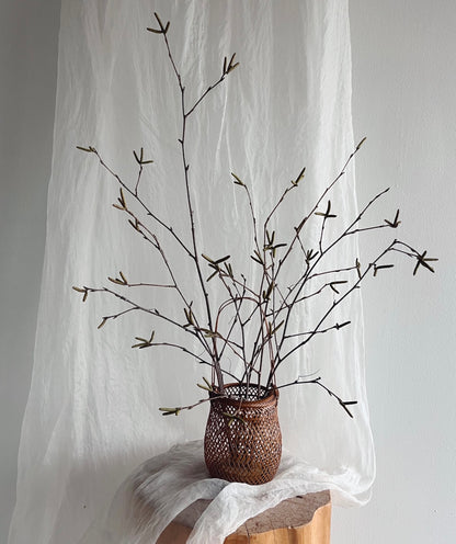 A small smoked bamboo basket with handle and dried branches. Basket handcrafted and hand woven by Japanese artist Mie Kodama.