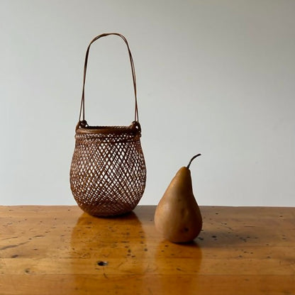 A small smoked bamboo basket handcrafted and hand woven by Japanese artist Mie Kodama. Shown next to a pear.