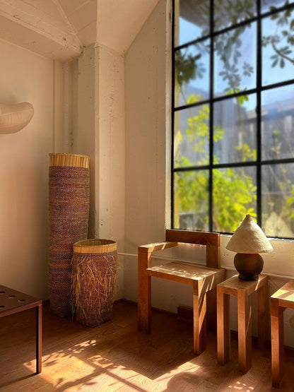 Tall floor standing storage baskets, natural colored with a shaggy textured exterior. Made in Ghana from local sustainable materials. Shown in a living room with chairs.