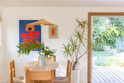 Sunhat light shade over a dining table. Light shade is woven into a shallow cone shape. Doorway into garden.