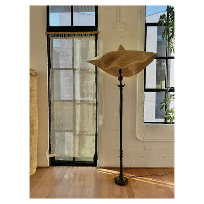 A vintage, iron 'Tête de femme' style floor lamp in the manner of Alberto Giacometti, paired with a Twenty One Tonnes handwoven, wide brimmed, natural colored light shade.