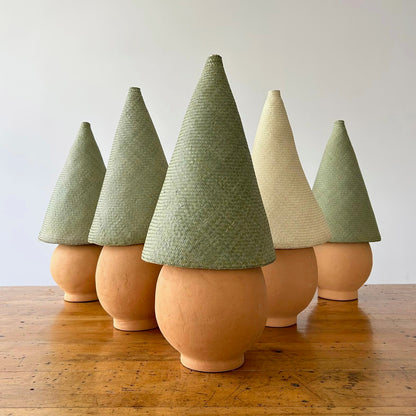 The Duende Lamp has a handcrafted, round, terracotta colored, ceramic base, with a natural colored, pointed cone shaped, hand woven, dried palm leaf lampshade. Shown here are five Duende lamps together