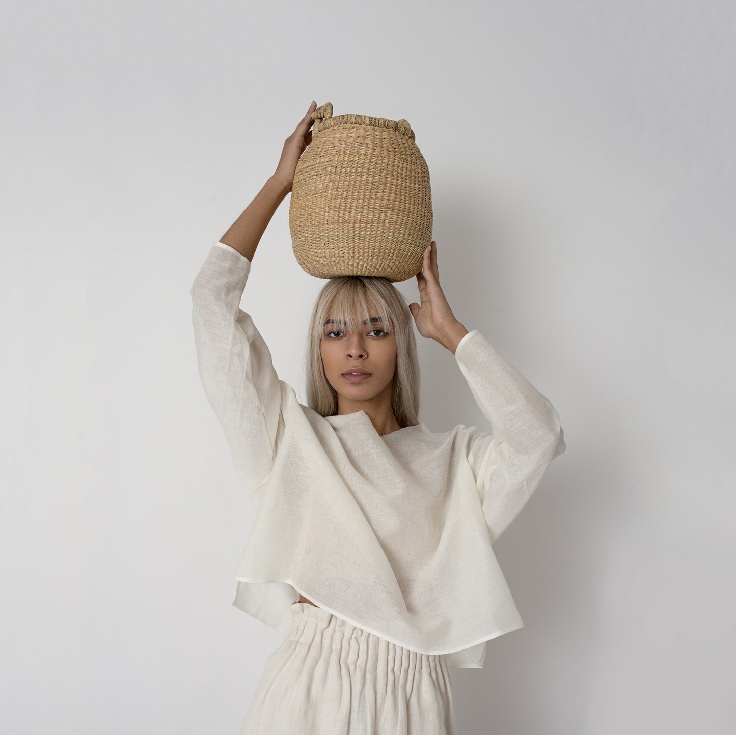 Woman resting a small handwoven basket on her head, made from natural colored elephant grass, from northern Ghana.