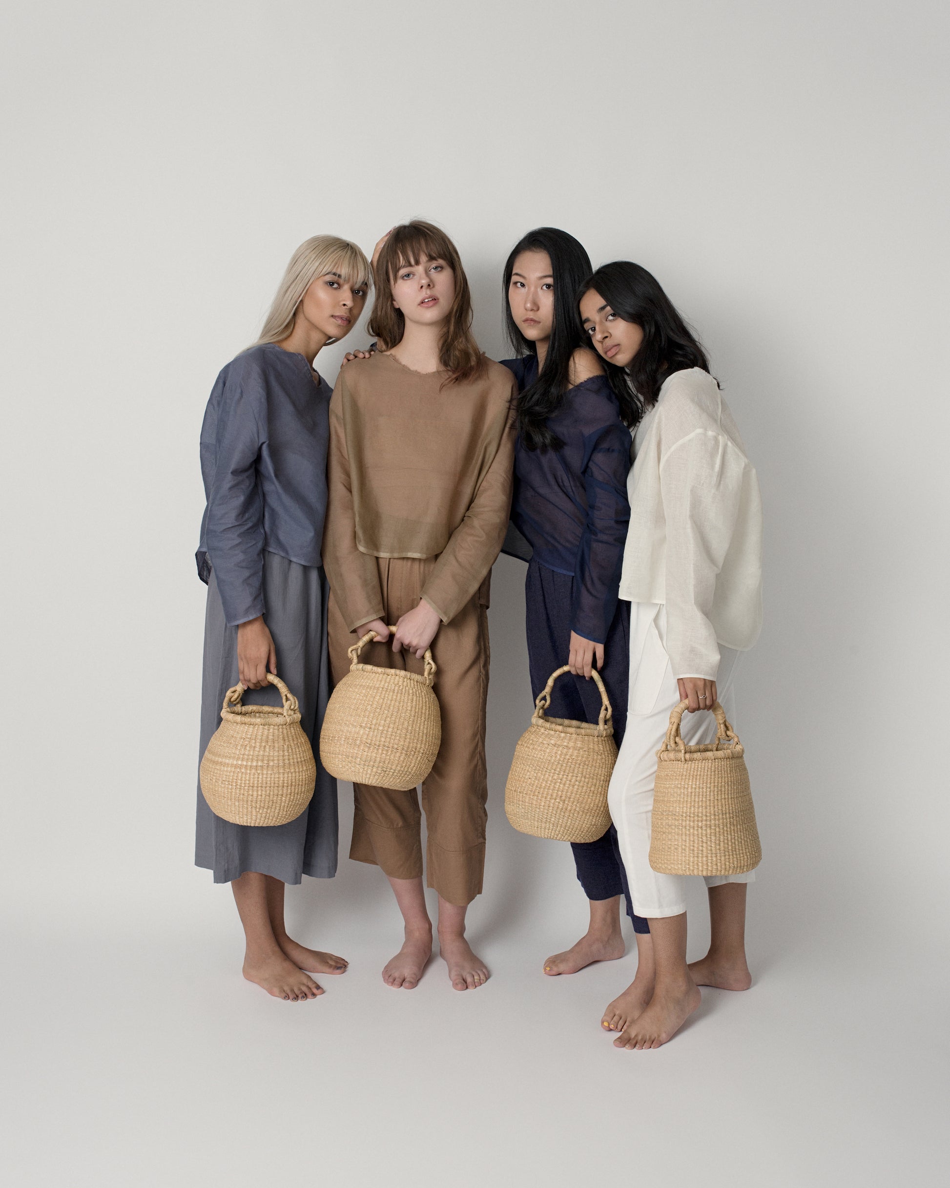 Women holding small handwoven baskets with handles, made from natural colored elephant grass.