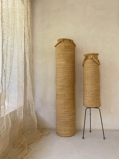 Very tall column-shaped baskets with two handles. More sculpture than storage, these hand woven baskets are made in Ghana from sustainable local grass.