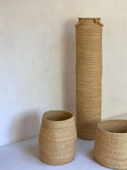 Very tall column-shaped basket with two handles, and two storage baskets.